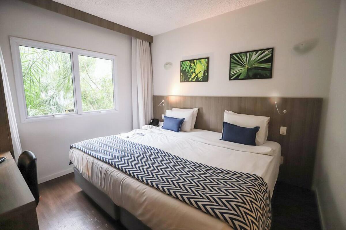 A neatly arranged hotel room with a large bed, a desk, and a window with curtains.