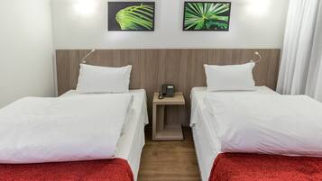 A hotel room with two single beds, a wooden headboard, a bedside table with a phone, and two wall-mounted pictures of leaves.