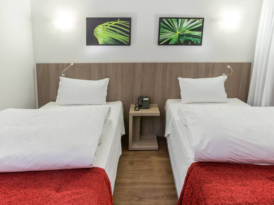 A hotel room with two single beds, a wooden headboard, a bedside table with a phone, and two wall-mounted pictures of leaves.