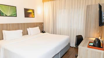 A hotel room with a large bed, a desk with a telephone, and a television on the wall.