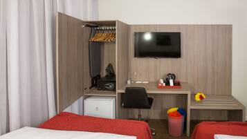 Habitación de hotel con dos camas, un escritorio, televisor, refrigerador pequeño, cafetera y un cubo de basura.