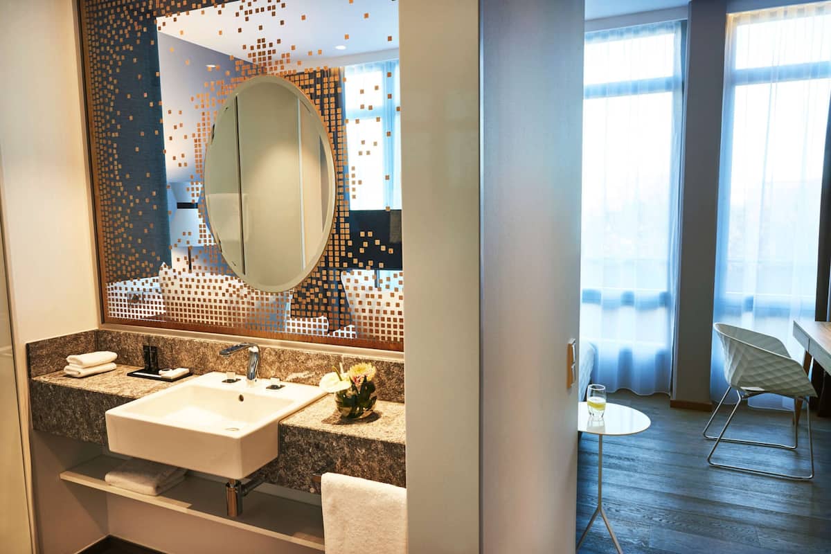 A modern bathroom with a large mirror, dual sinks, and a small table with a glass of water.