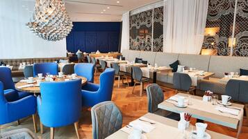 Ein modernes Restaurant mit blauen und grauen Sitzgelegenheiten, Holztischen und einem dekorativen Kronleuchter.