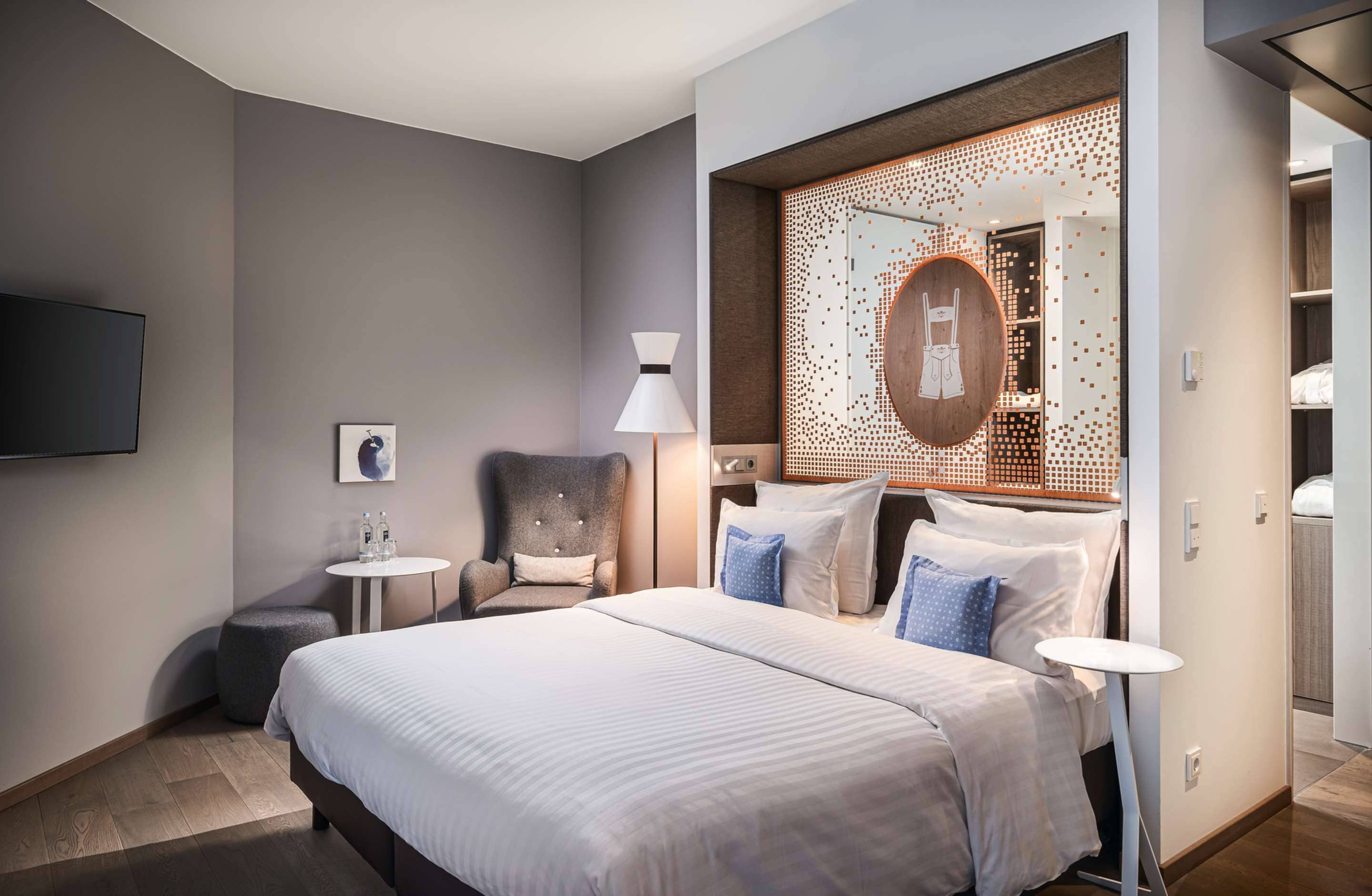 Una habitación de hotel moderna con una cama grande, un escritorio, una silla, un espejo redondo y una pequeña mesa.