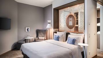 Una habitación de hotel moderna con una cama grande, un escritorio, una silla, un espejo redondo y una pequeña mesa.