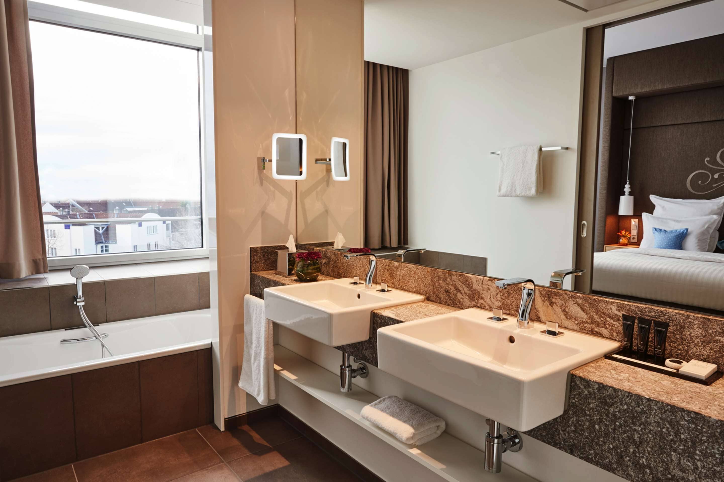 Une salle de bain moderne avec deux lavabos, un grand miroir et une fenêtre donnant sur la ville.