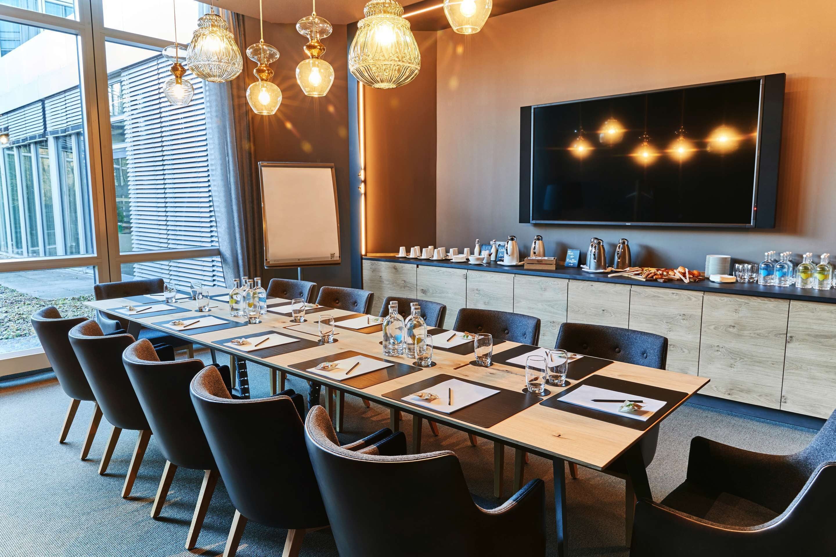 A conference room with a long table, chairs, a TV, and a bar area with various items.