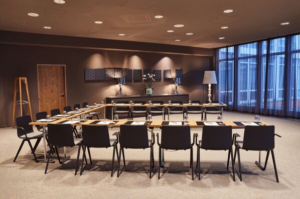 A conference room with a long table, black chairs, and a large window. - Steigenberger Hotel München (Munich)