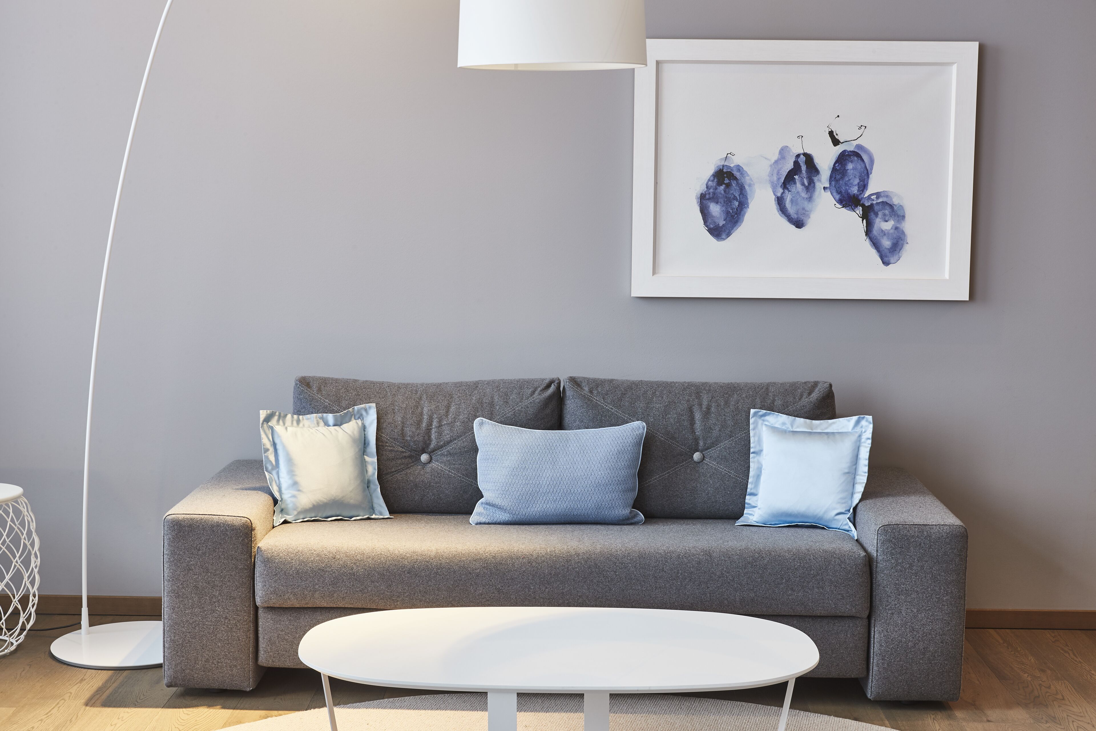 A modern living room with a grey sofa, two blue pillows, a white coffee table, and a framed artwork on the wall.