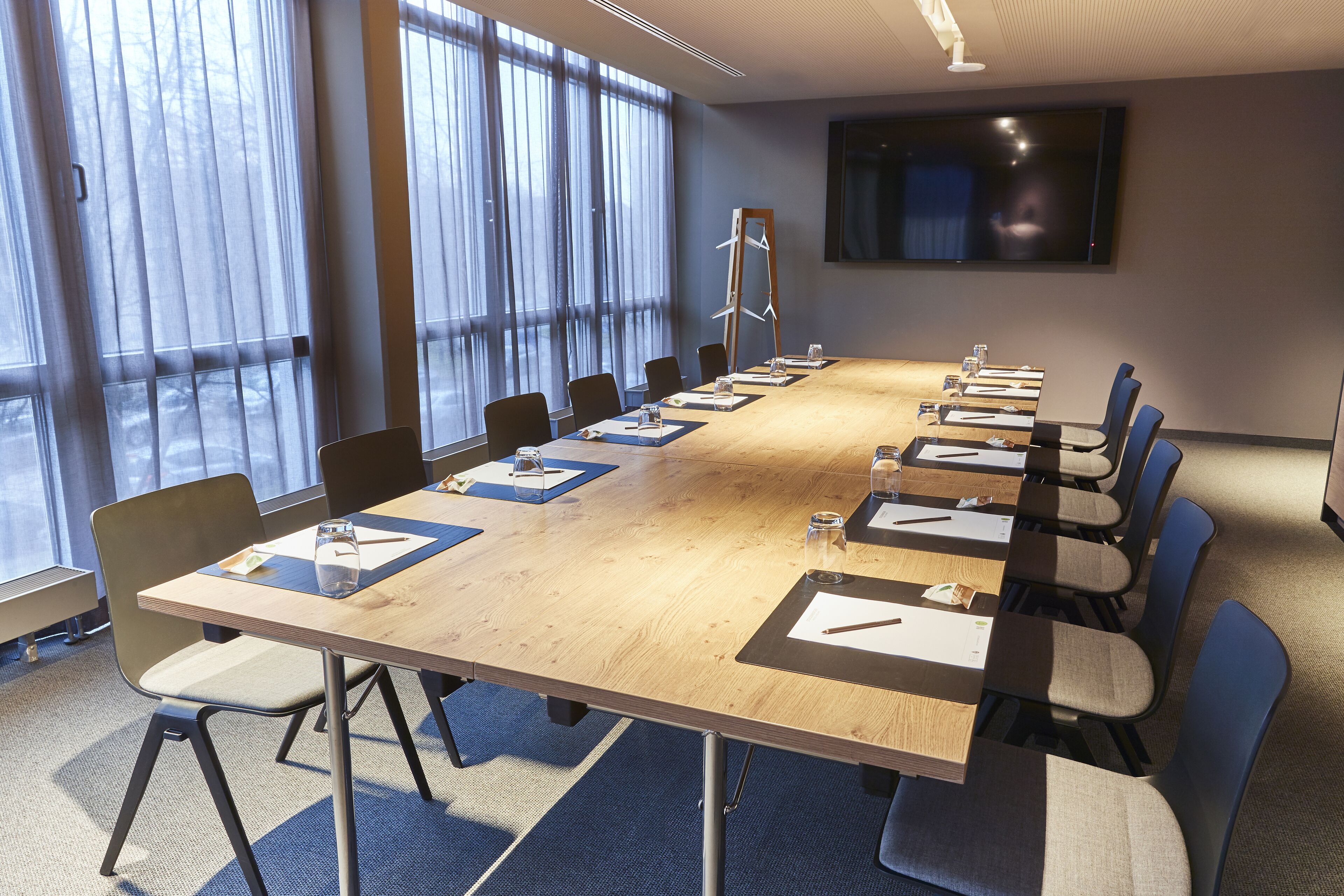 A conference room with a long table, chairs, and a TV screen on the wall.