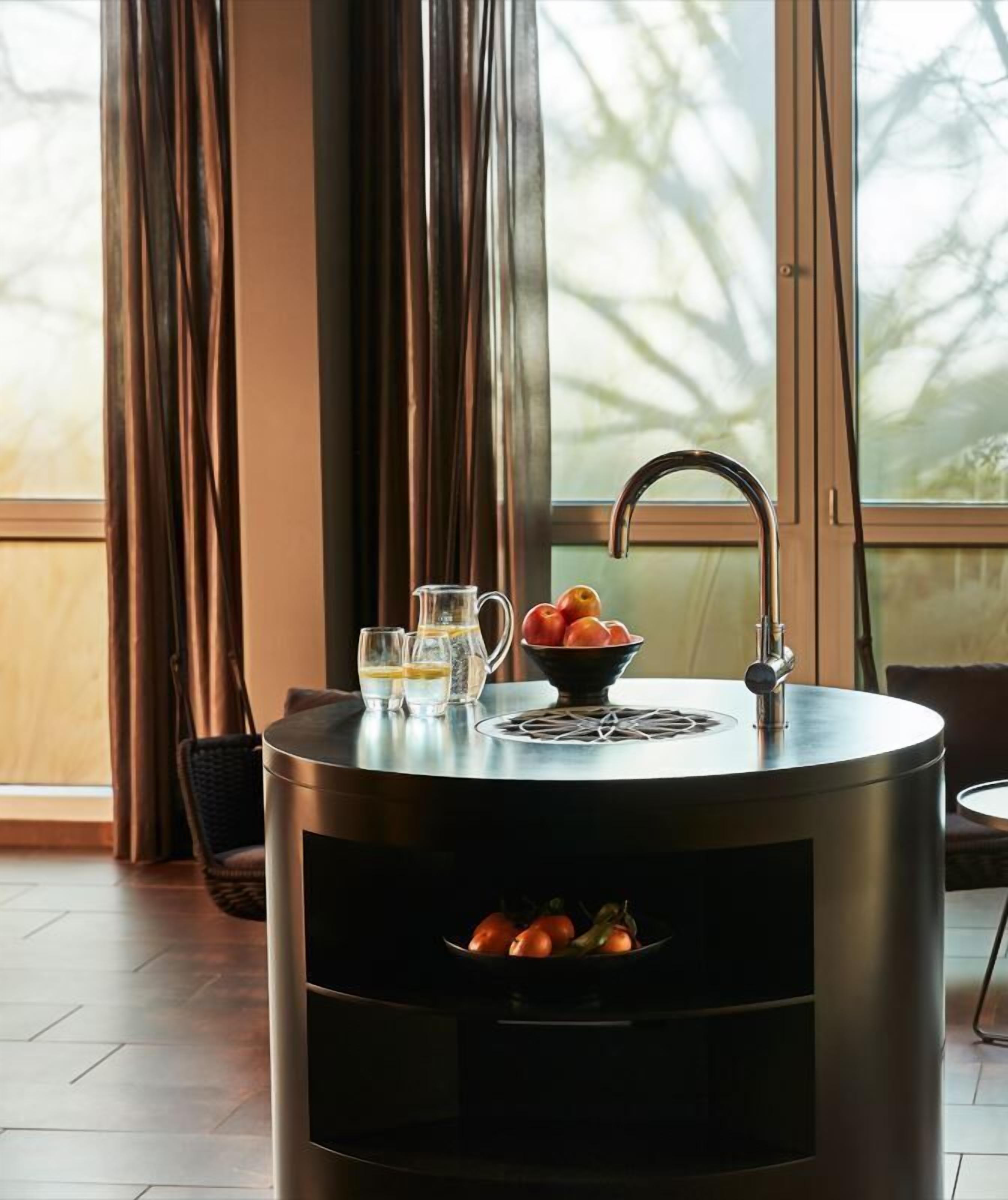 A modern kitchen with a round stove, a sink, and a window with curtains.