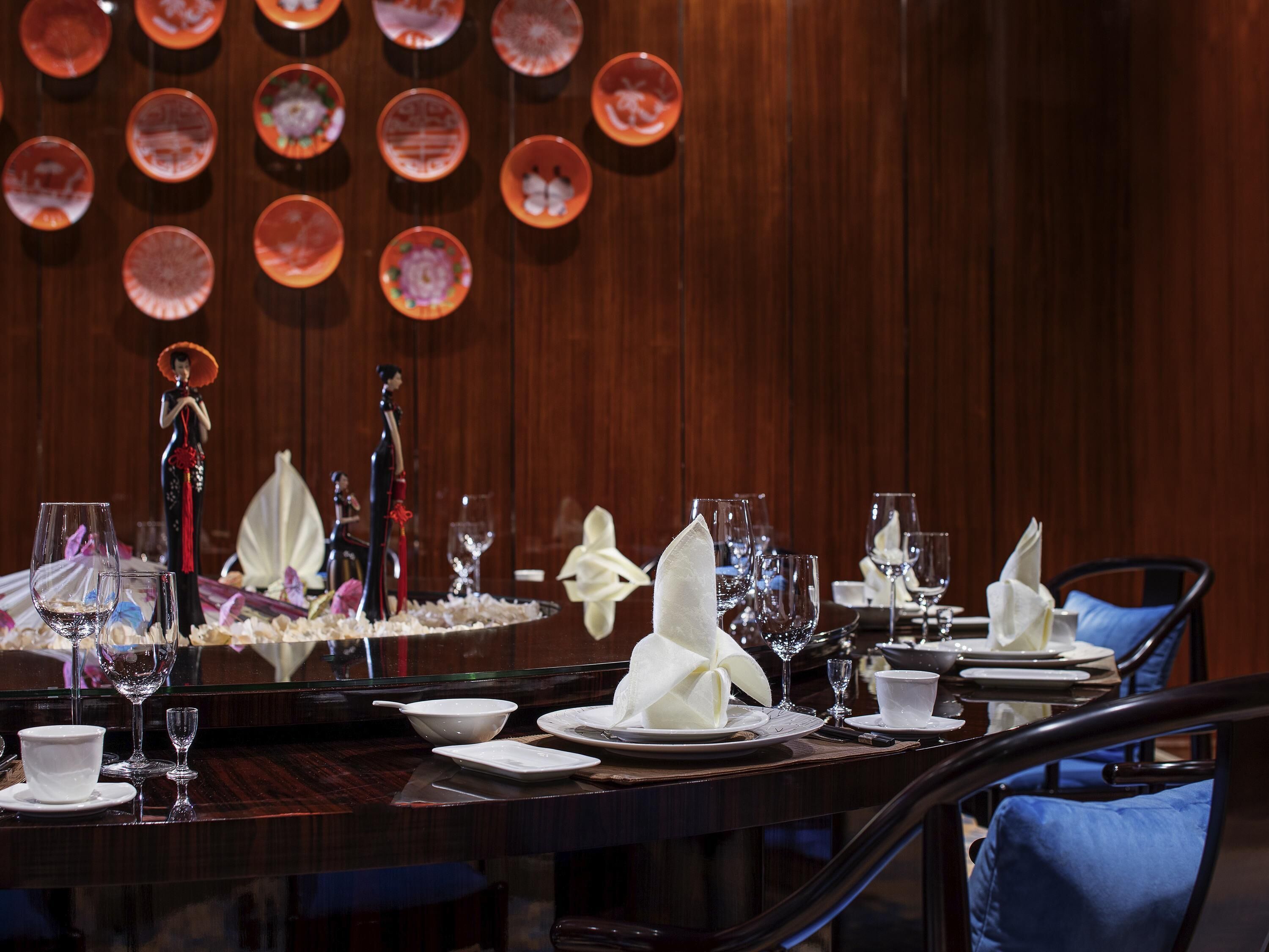 A dining area with a long table set for a meal, a decorative wall with circular patterns, and a statue in the background.