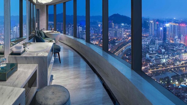 Une salle de bain moderne au design épuré, dotée d’une baignoire et d’une grande fenêtre offrant une vue sur la ville.