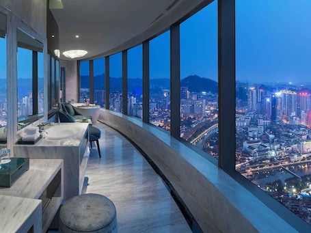 A modern bathroom with a curved design, a bathtub, and a large window offering a city view.. Sofitel Guiyang Hunter