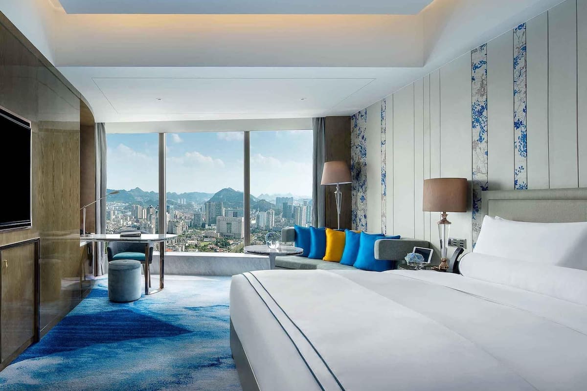 Une chambre d’hôtel avec un grand lit, un bureau, une chaise, une télévision et une vue sur le paysage urbain.
