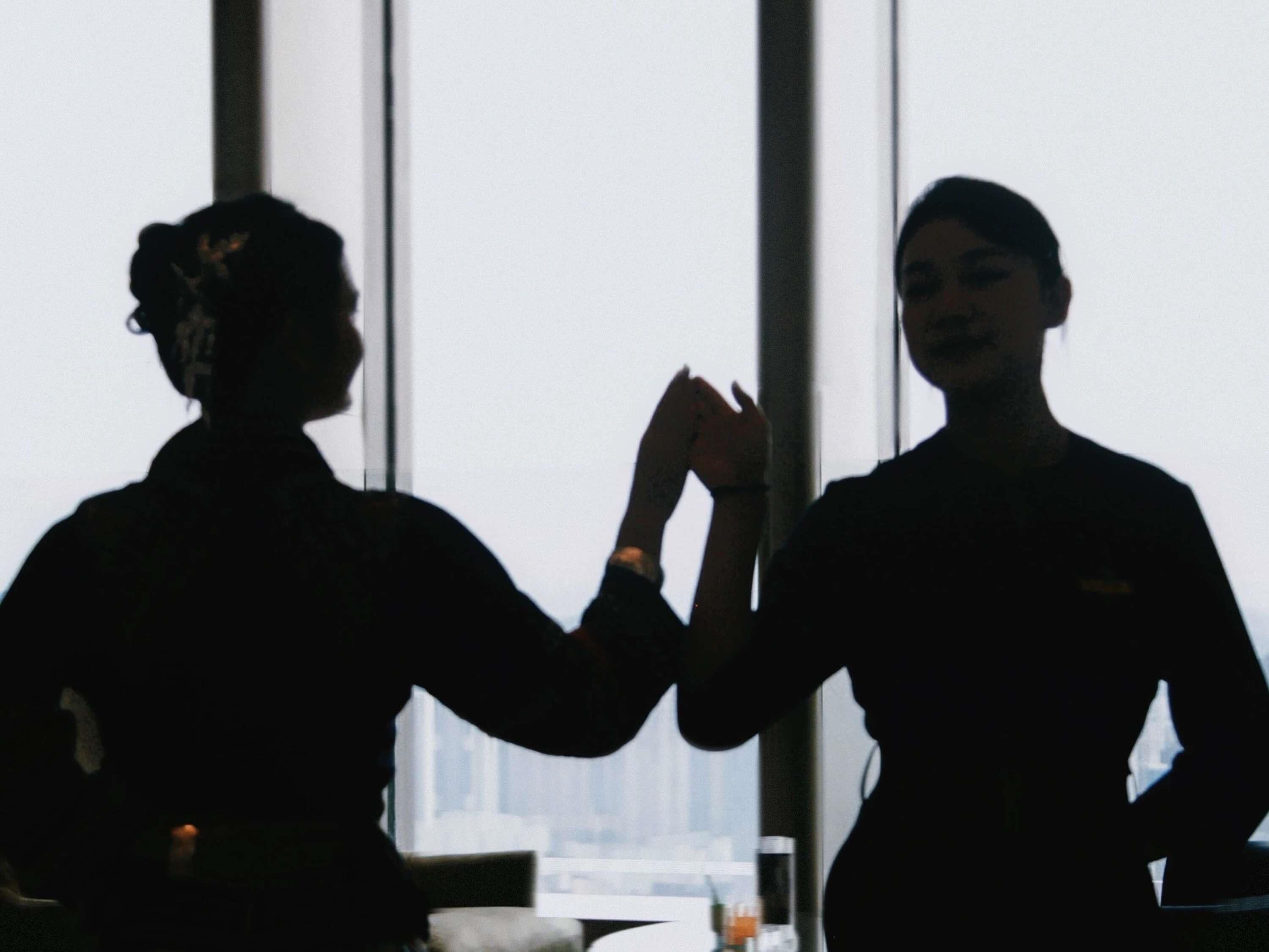 Two silhouettes of people in a room with large windows.
