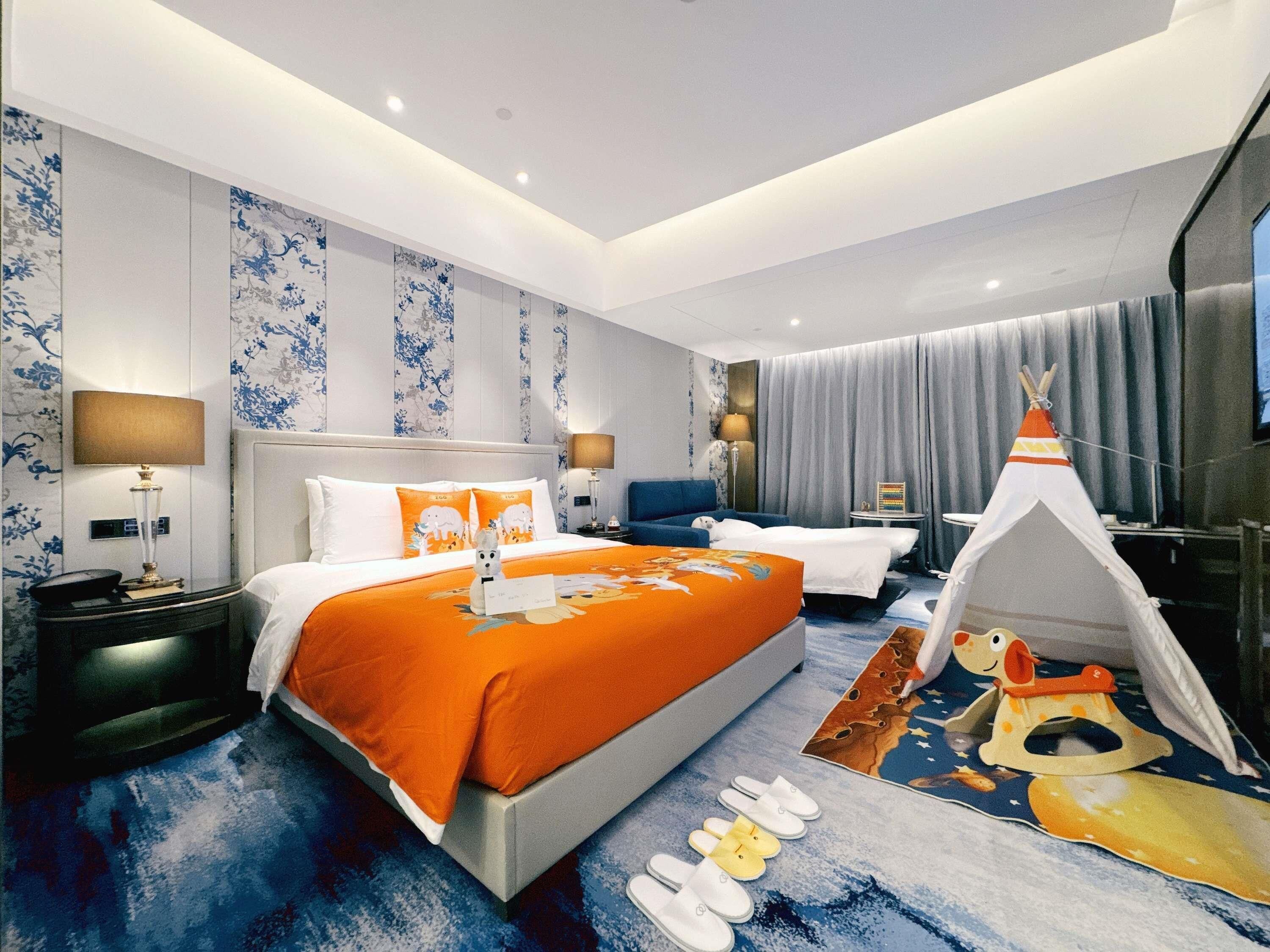 Een hotelkamer met een groot bed, een nachtkastje, een bureau, een stoel, een lamp, een televisie, een raam met gordijnen en een tipi decoratie.