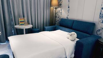 A hotel room with a bed, a blue sofa, a round table with a lamp, and a colorful abacus.