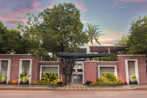 Un edificio de ladrillo con una entrada cubierta, rodeado de exuberante vegetación y palmeras.