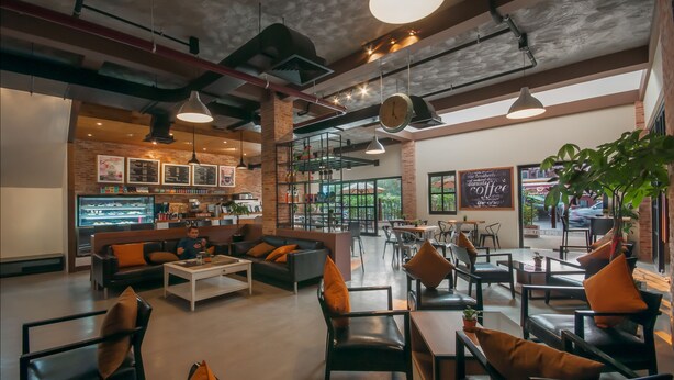 A modern cafe with a brick wall, wooden beams, and a mix of seating options including sofas and tables. - The Privilege Boutique (Siem Reap)