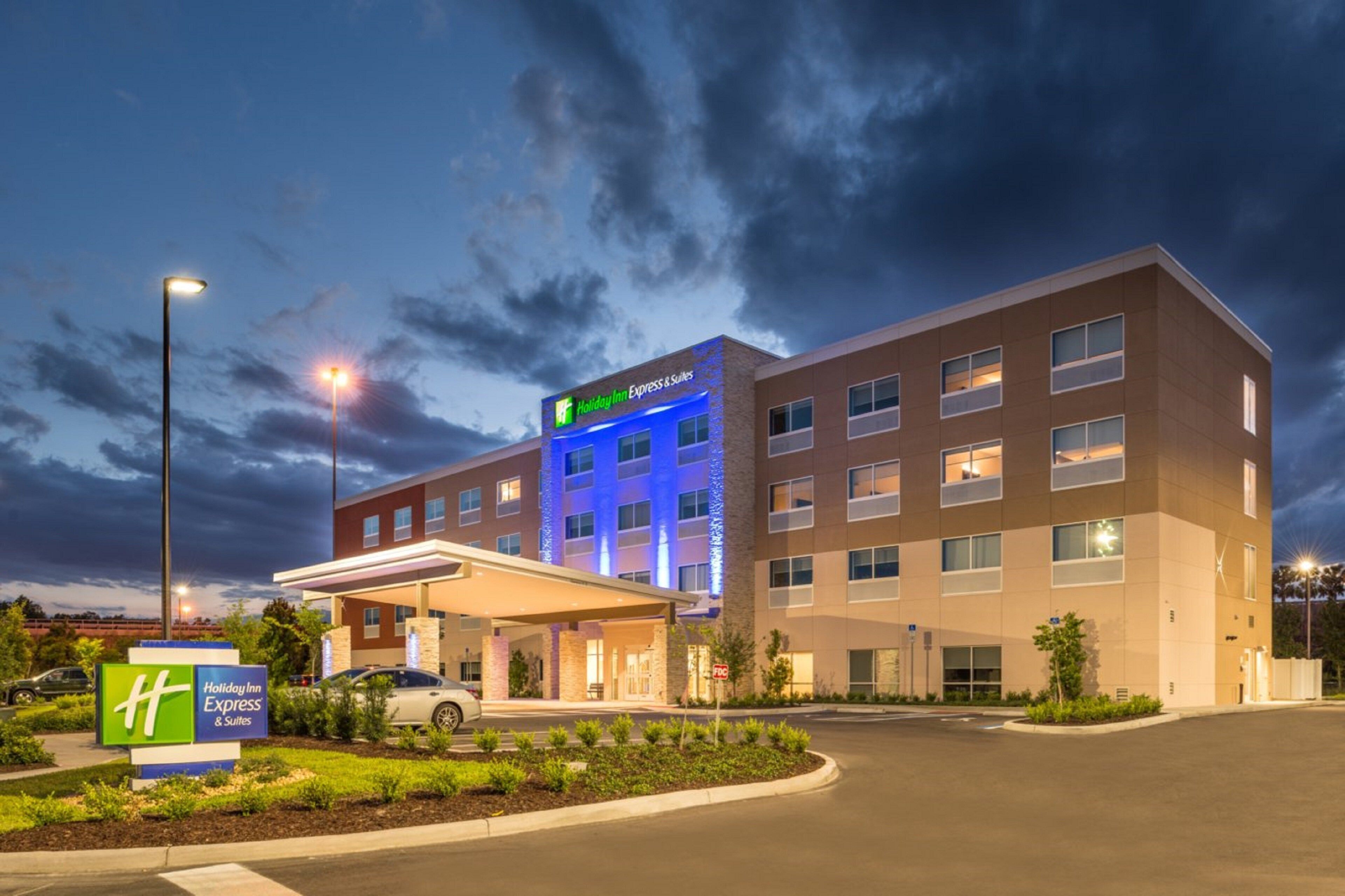 A Holiday Inn Express & Suites hotel with a modern design, featuring a covered entrance and a well-lit facade.
