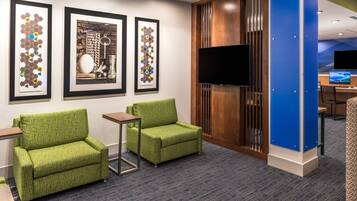 A hotel lobby with two green armchairs, a wooden partition, and three framed artworks on the wall.
