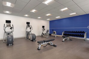 Un gimnasio con diversos equipos de ejercicio, incluyendo cintas de correr, una elíptica y una prensa de banca.