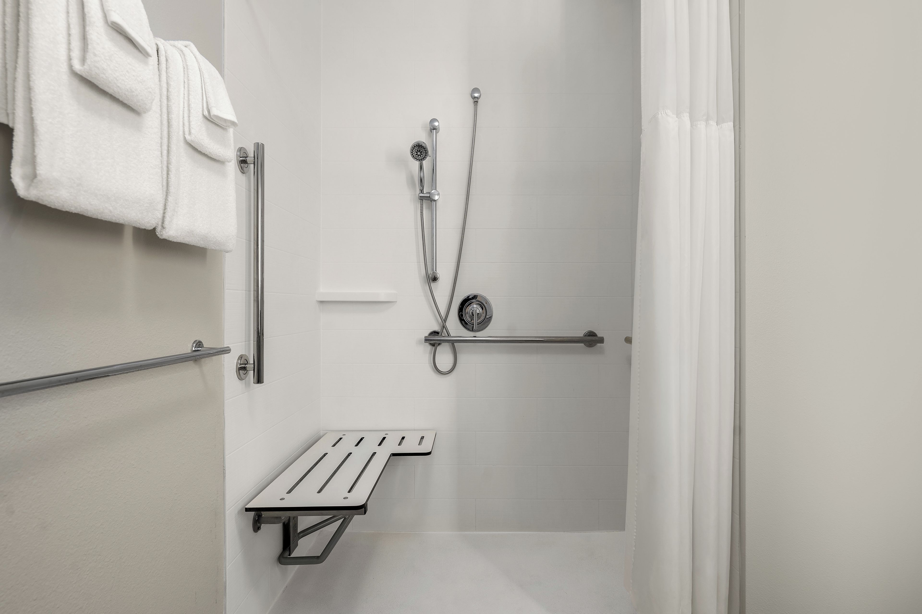A shower area with a handheld showerhead, a handheld shower attachment, and a towel rack with a white towel.