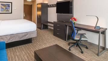 Habitación de hotel con cama, escritorio, silla, televisor y una mesita.