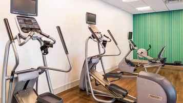 An indoor fitness area with treadmills and elliptical machines, equipped with digital displays, in a room with wooden flooring and a green curtain.