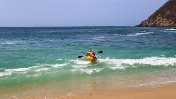 Um caiaqueiro num caiaque amarelo numa praia com água transparente e um penhasco rochoso ao fundo.