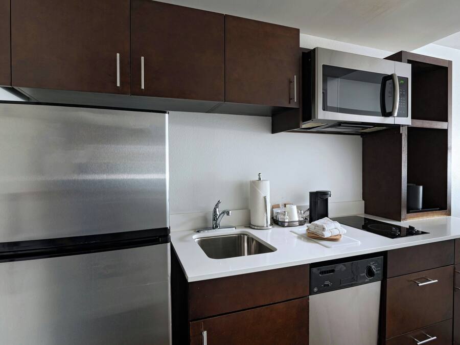 A modern kitchen with stainless steel appliances, dark wooden cabinets, and a white countertop.