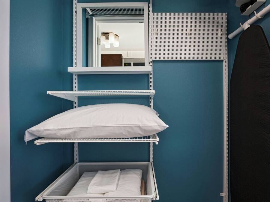 A compact room with a bunk bed, a mirror, a drying rack, and a black ironing board.