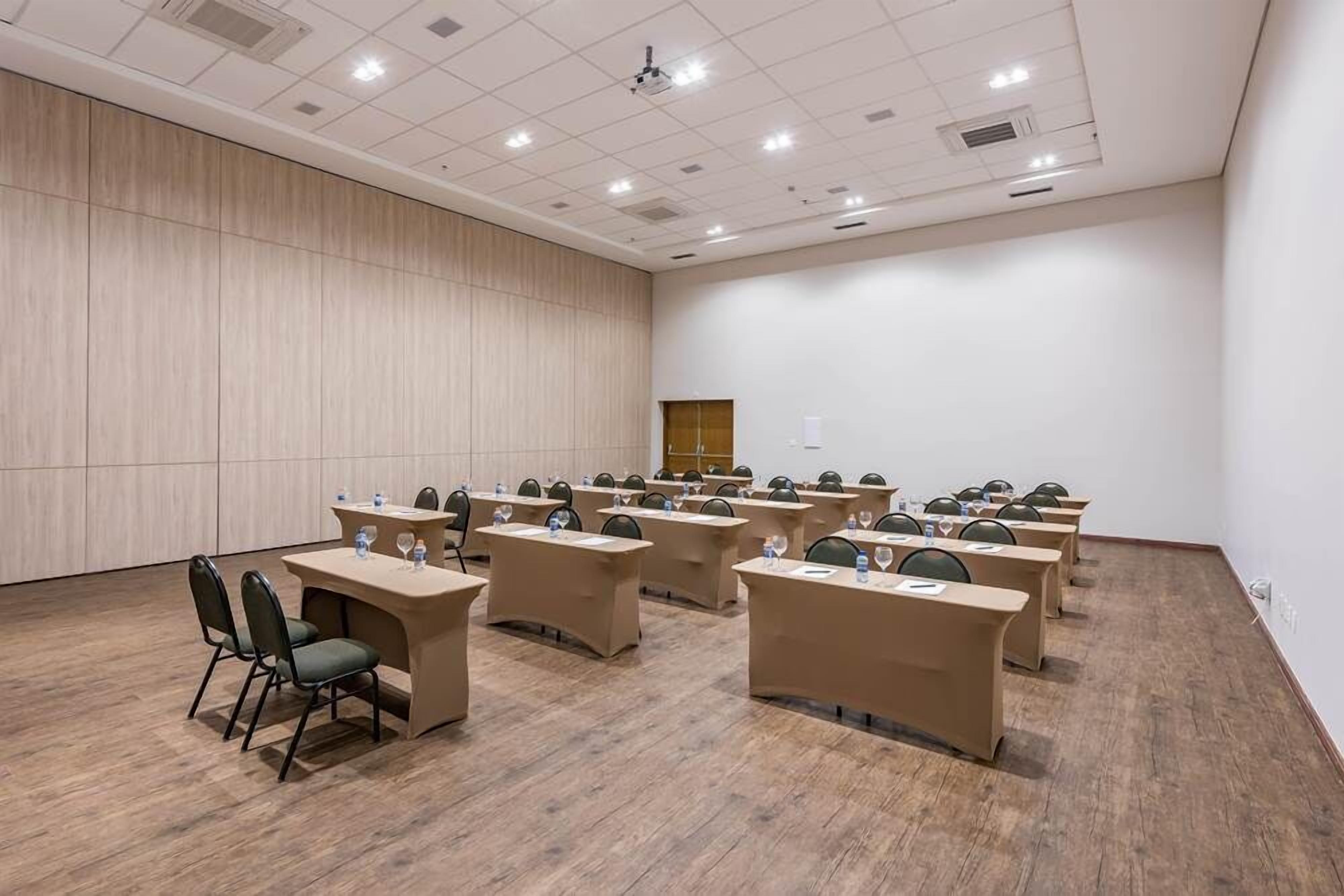A conference room with multiple tables and chairs, a wooden panel wall, and a projector screen.