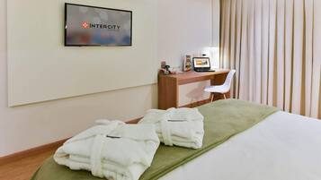 A hotel room with a bed, a desk with a computer, and a TV displaying the hotel name.