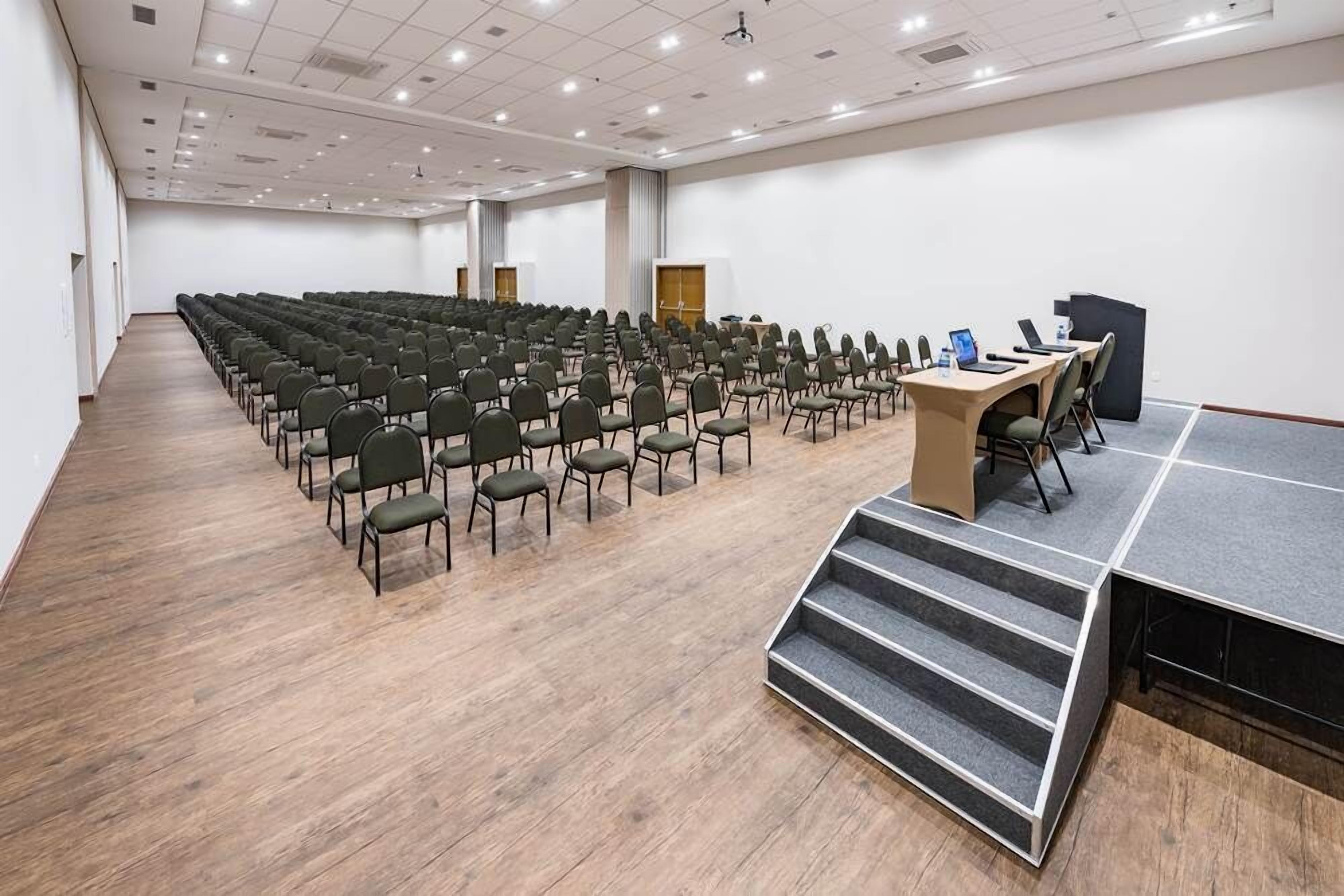A conference room with rows of chairs, a stage with a podium, and a carpeted staircase.