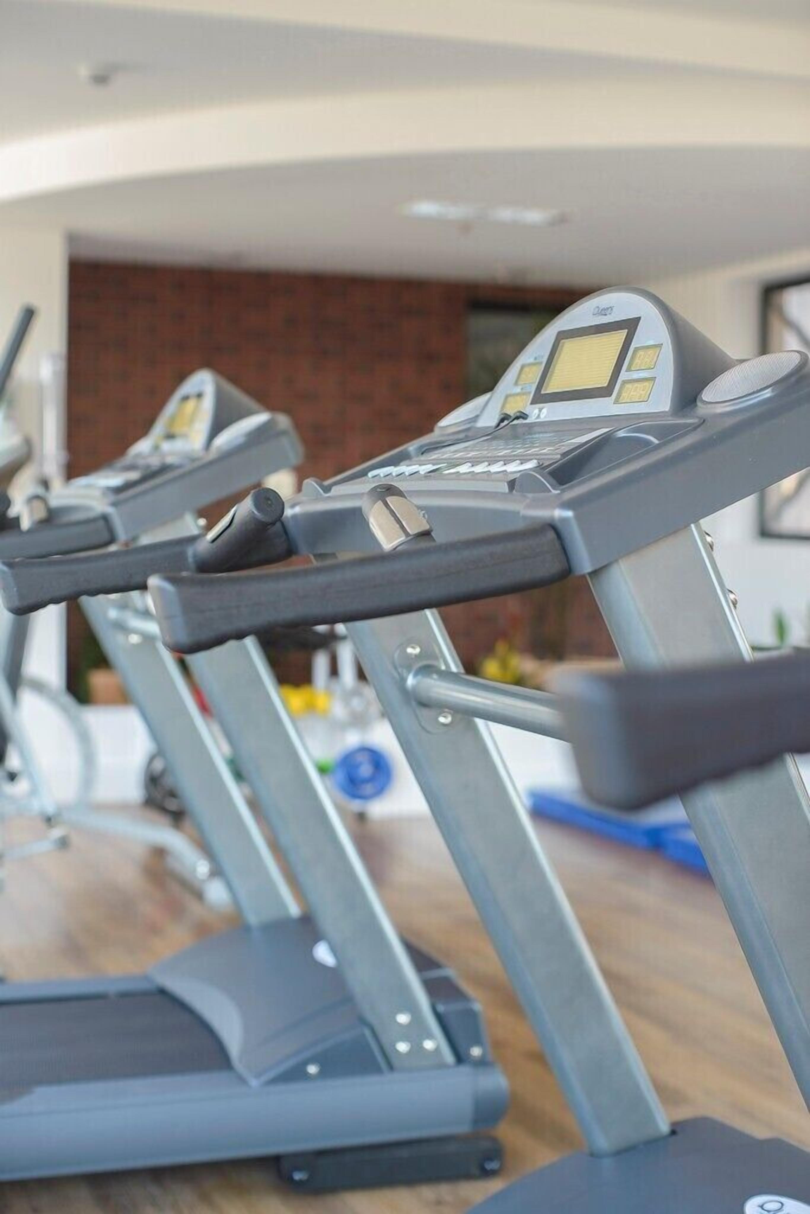 Una hilera de cintas de correr en un gimnasio, cada una con una pantalla digital.