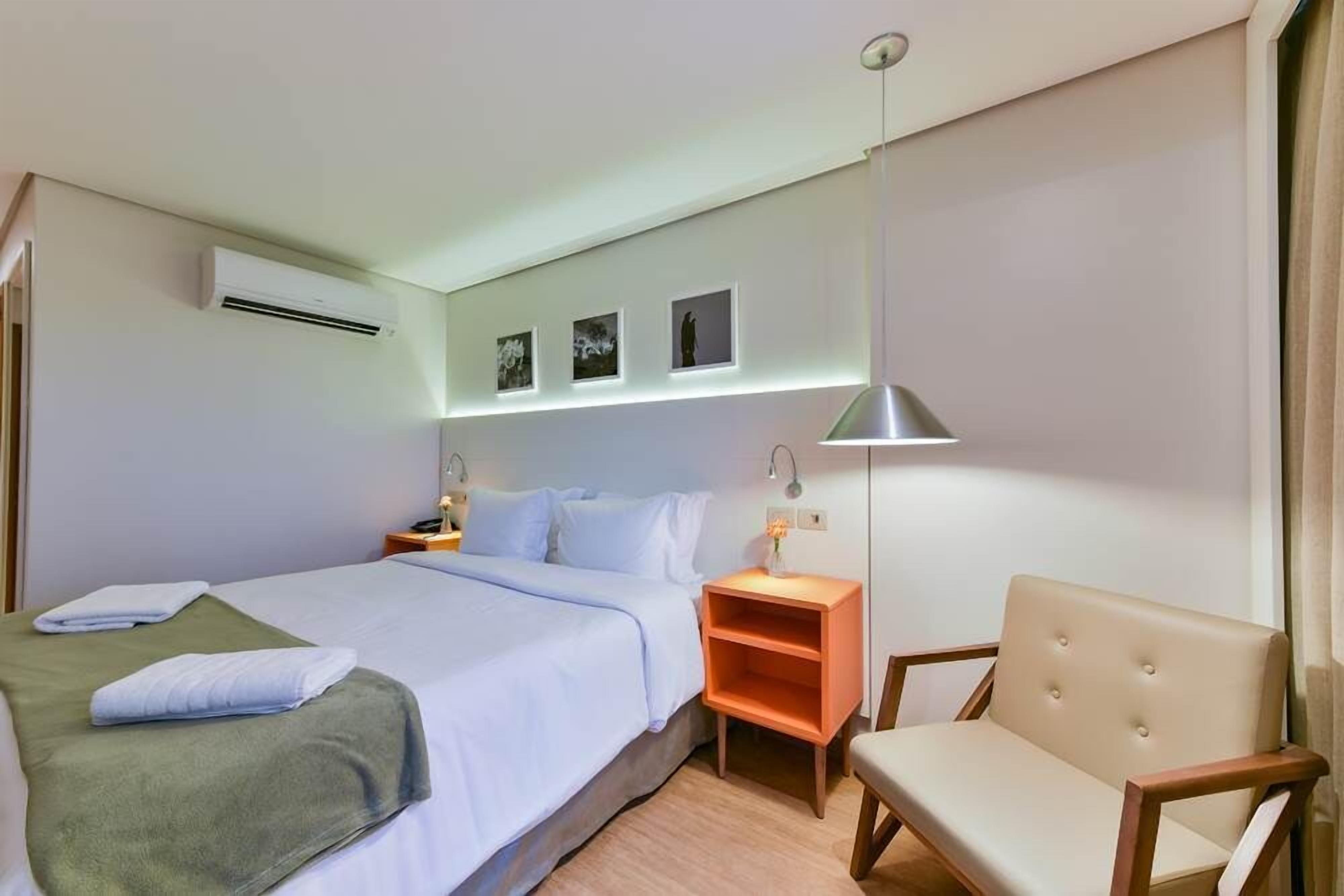 Habitación de hotel con cama, una silla, una mesita de noche y aire acondicionado instalado en la pared.