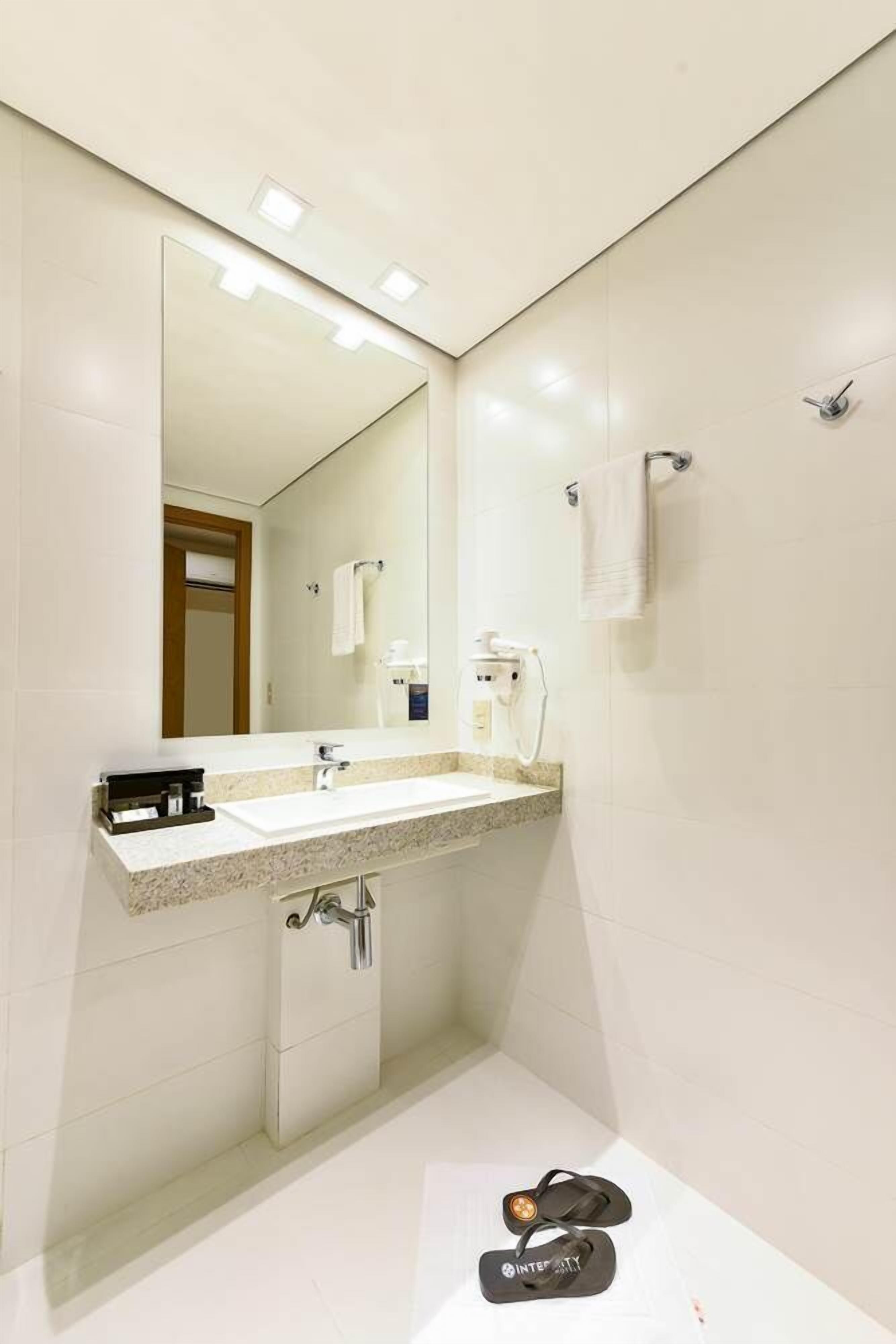 A modern bathroom with a large mirror, white tiles, a sink, and a shower.