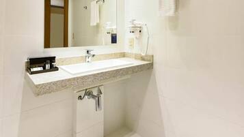 A modern bathroom with a large mirror, white tiles, a sink, and a shower.