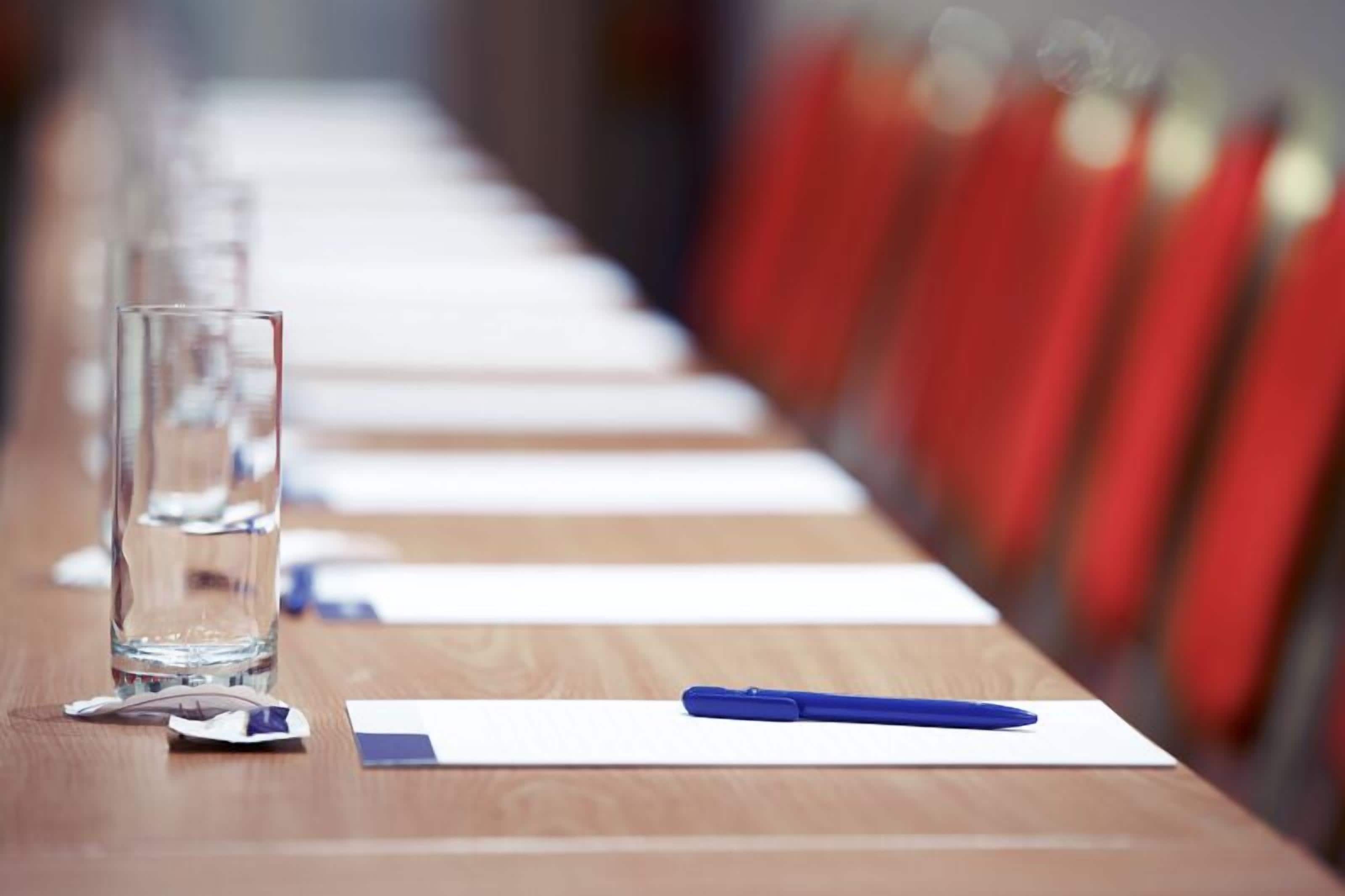 Une table de conférence avec un verre d’eau, un stylo et des papiers.