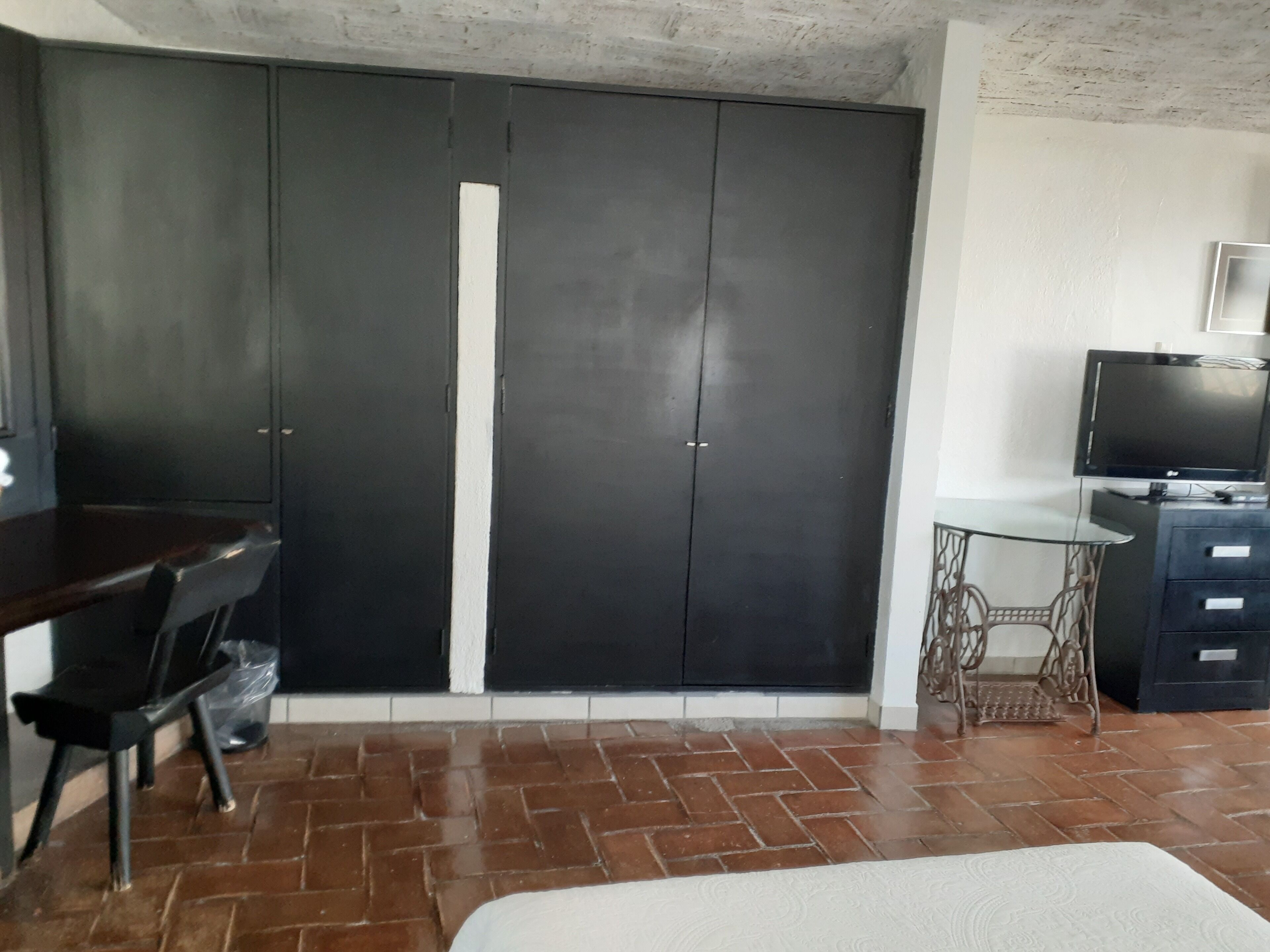 A room with a large wardrobe, a desk with a chair, a television, and a small table.