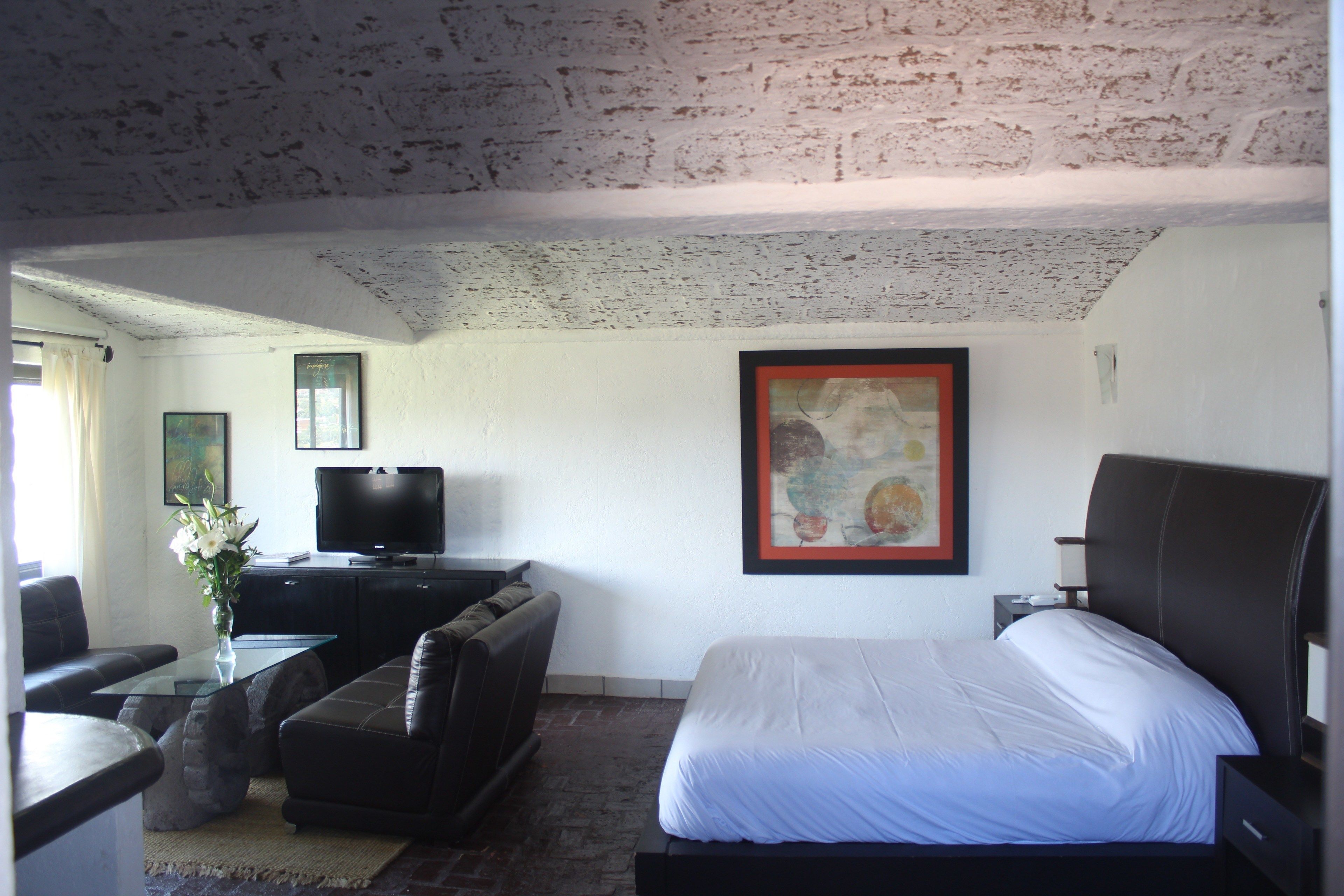 A hotel room with a bed, a television, a sofa, and a painting on the wall.