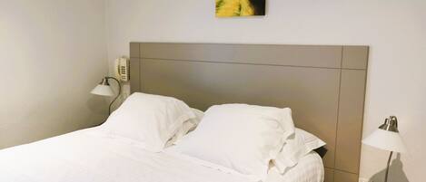 A neatly made bed with white linens in a hotel room.