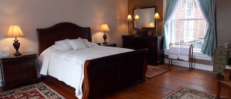 A neatly arranged bedroom with a large bed, two bedside tables with lamps, a dresser, and a window with curtains.