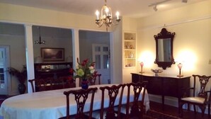 Comedor con una mesa dispuesta para seis comensales, rodeada de sillas de madera. Un candelabro cuelga del techo, y un espejo está colocado en la pared.