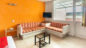 Una habitación con un sofá blanco, una mesita, un televisor en la pared y un ventanal con vistas al exterior.