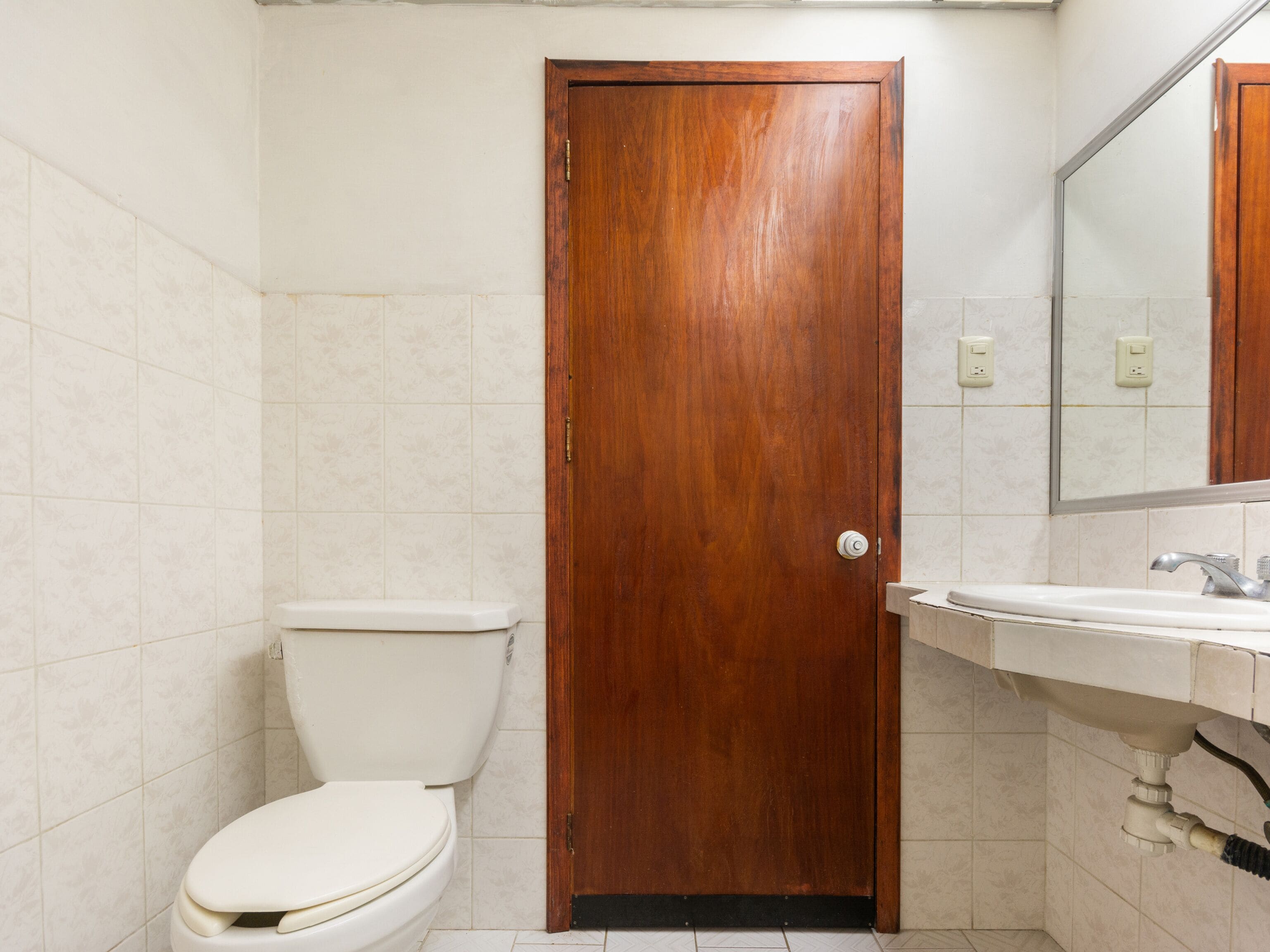 Un baño con puerta de madera, un inodoro y un lavabo con un espejo encima.
