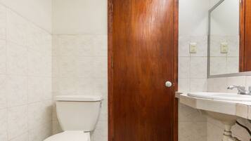 Un baño con puerta de madera, un inodoro y un lavabo con un espejo encima.