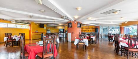 Un restaurante espacioso con varias mesas y sillas, suelo de baldosas y un ambiente luminoso.